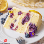 A mouthwatering Blueberry Lemon Creme Cake, exuding homemade perfection. The cake, adorned with luscious blueberries, features a velvety creme layer and a sprinkle of fresh lemon zest. The golden-brown masterpiece promises a symphony of flavors in every bite, inviting you to savor the delicious combination of blueberries and citrus.