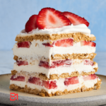 A mouthwatering image of a luscious Strawberry Refrigerator Cake, showcasing layers of fresh strawberries, creamy whipped filling, and graham crackers. The vibrant red of the strawberries contrasts beautifully with the velvety cream, inviting you to indulge in a delightful slice of this heavenly dessert. The perfect combination of simplicity and flavor, this cake is a visual feast for any occasion.