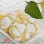 Homemade lemon cookies coated in powdered sugar on a baking sheet.