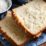 A mixing bowl with coconut bread ingredients like shredded coconut and flour.