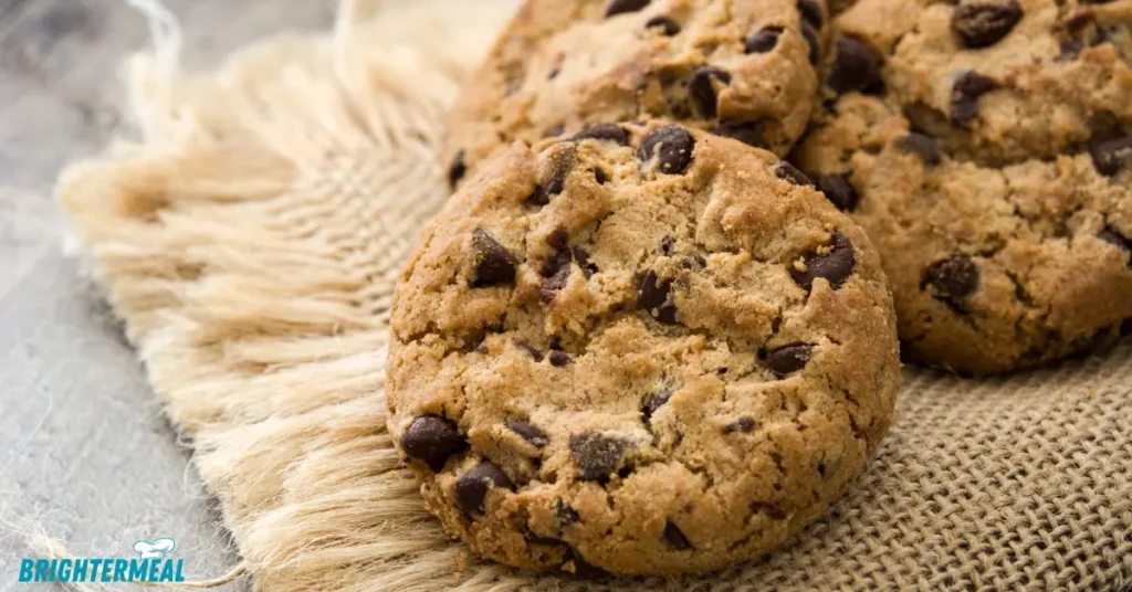 Peanut butter jar and chocolate chips with cookies in the background.